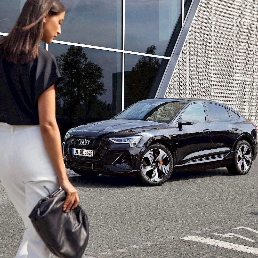 Woman walking to a black Audi in front of a modern building